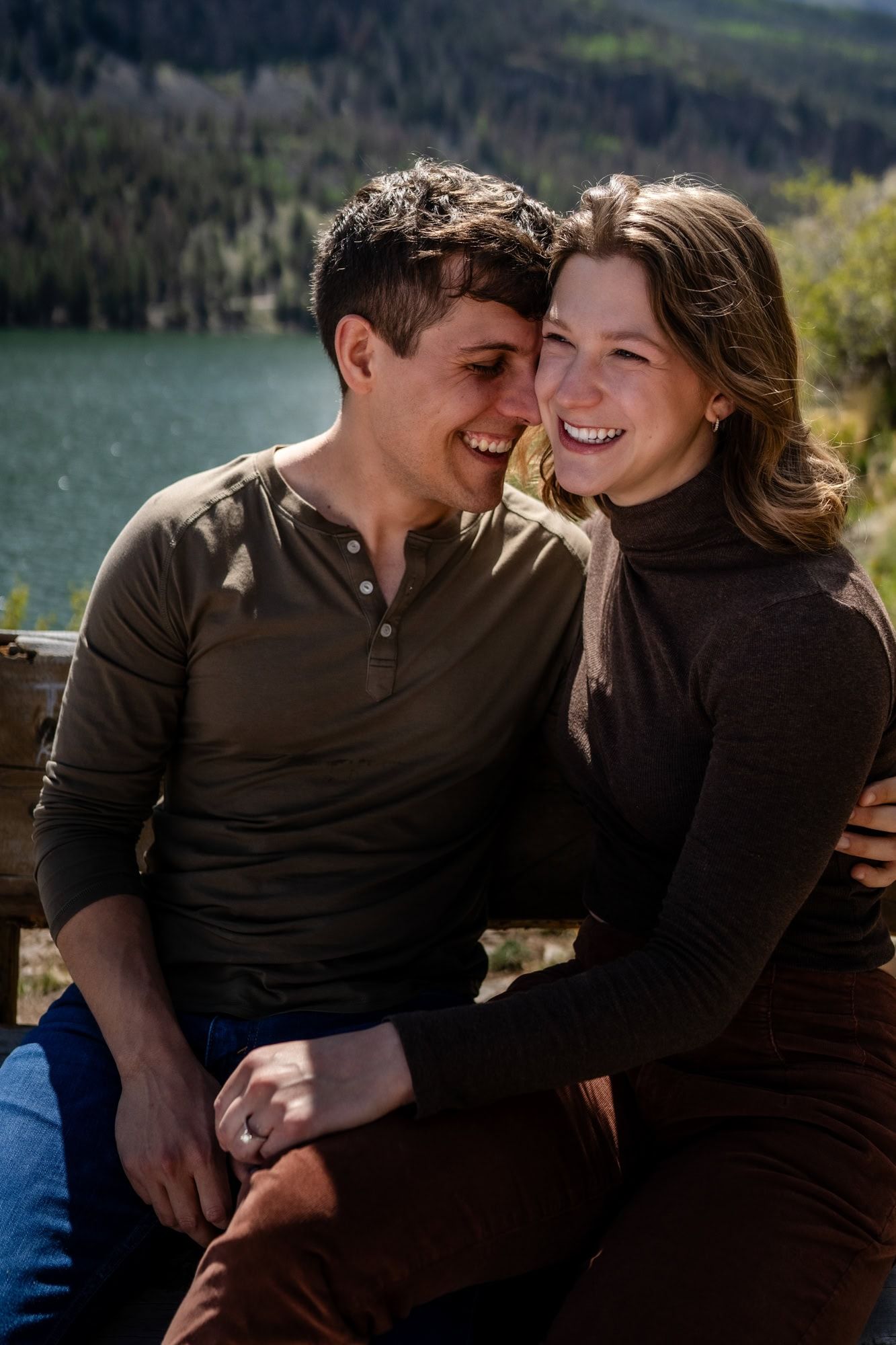 A candid moment of a couple laughing together by a scenic mountain lake.