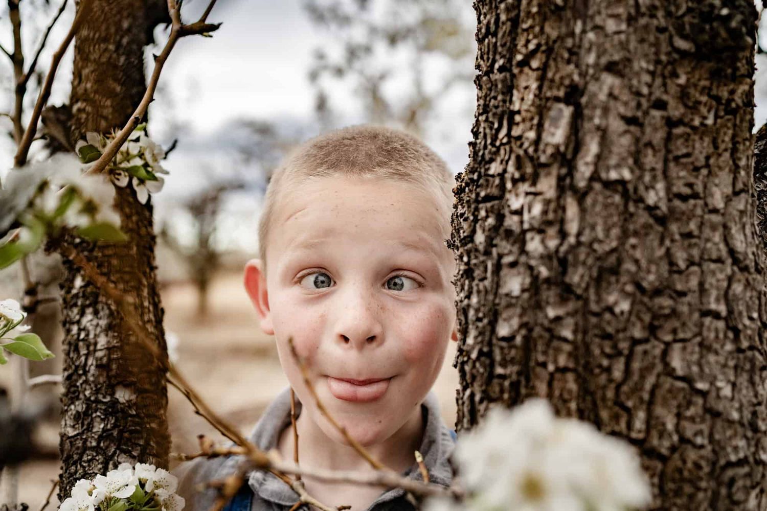Playful child peeking out from behind tree trunk with silly expression.