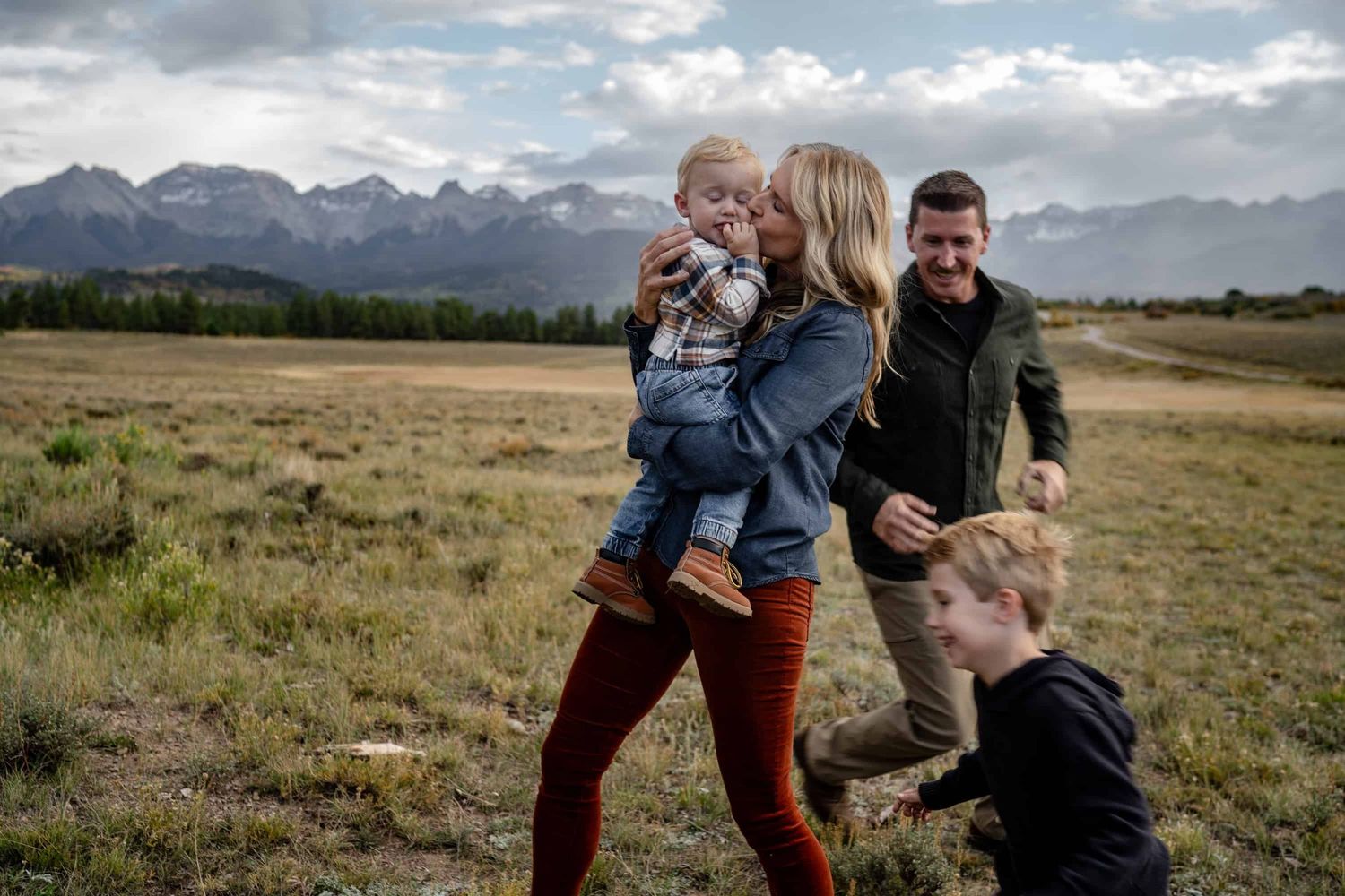 Family playing and laughing together in mountain field with dramatic sky. Taken by a photographer in Montrose Colorado.