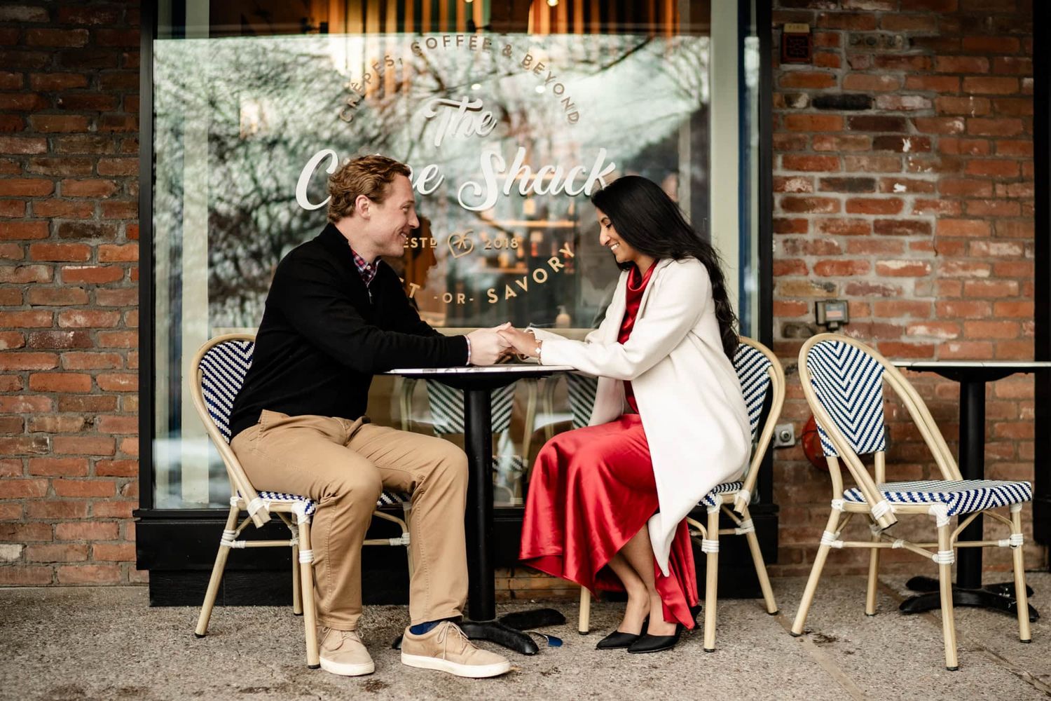 A couple sharing an intimate conversation at an outdoor cafe table with brick wall backdrop.