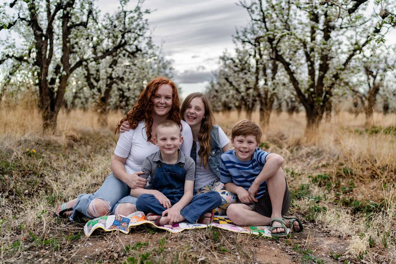 Family sitting together on a blanket in an autumn field surrounded by trees.