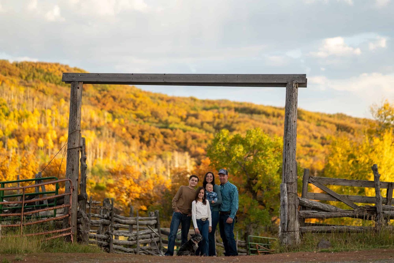 Group stands under wooden ranch gate frame with golden autumn hillside in background.