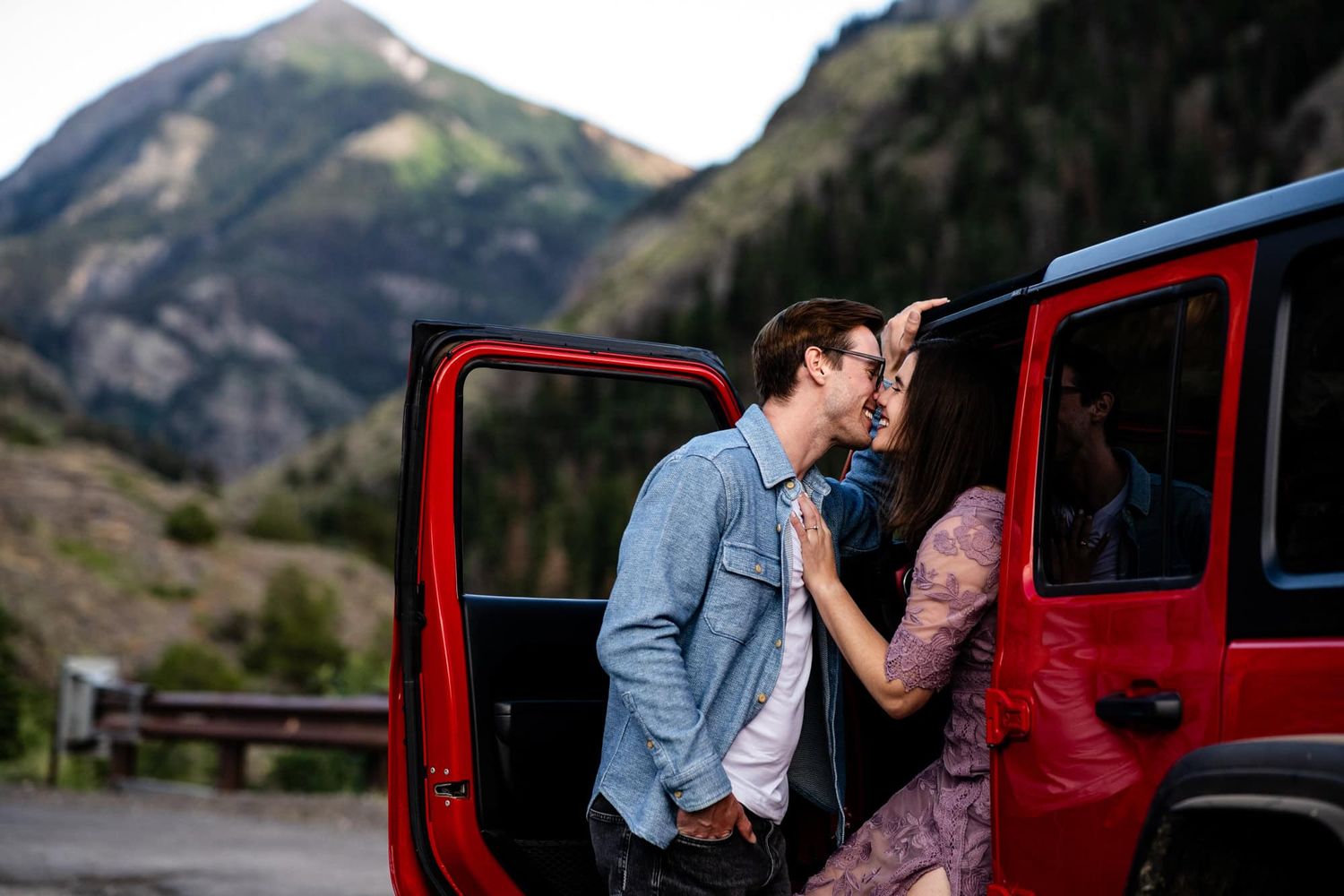 Couple shares kiss in red jeep with Mount Abrams behind them. Captured by Ouray Colorado Wedding Photographers