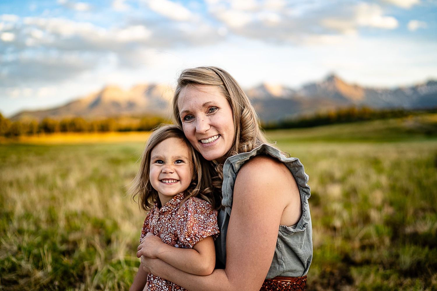 Parent and child embrace while standing in mountain meadow at sunset.
