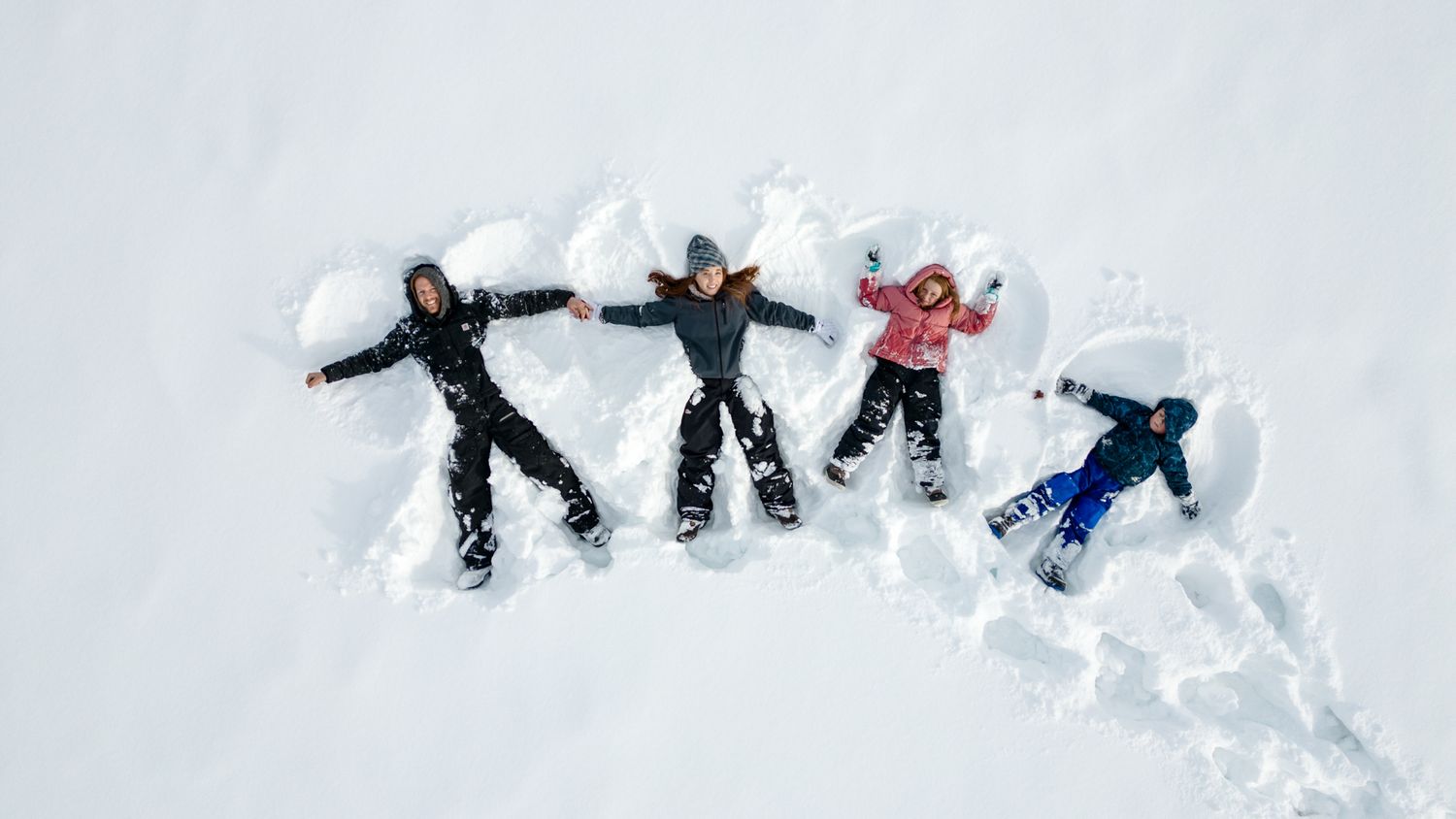 Four people making snow angels together in fresh powder snow viewed from above.
