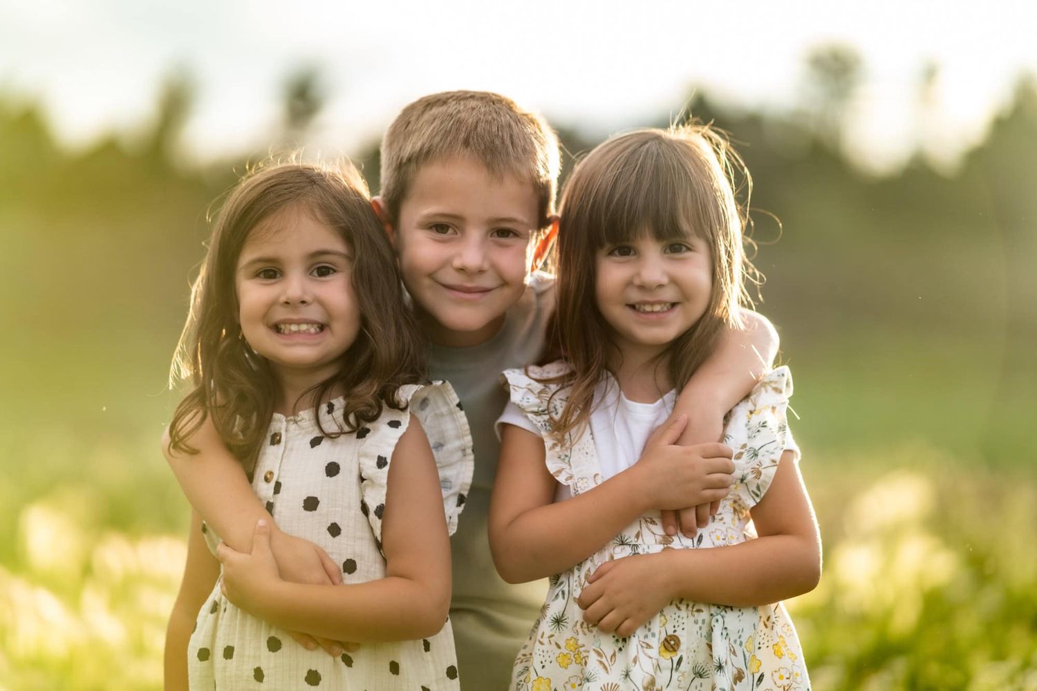 Three young people embracing and smiling together in a sunlit field.