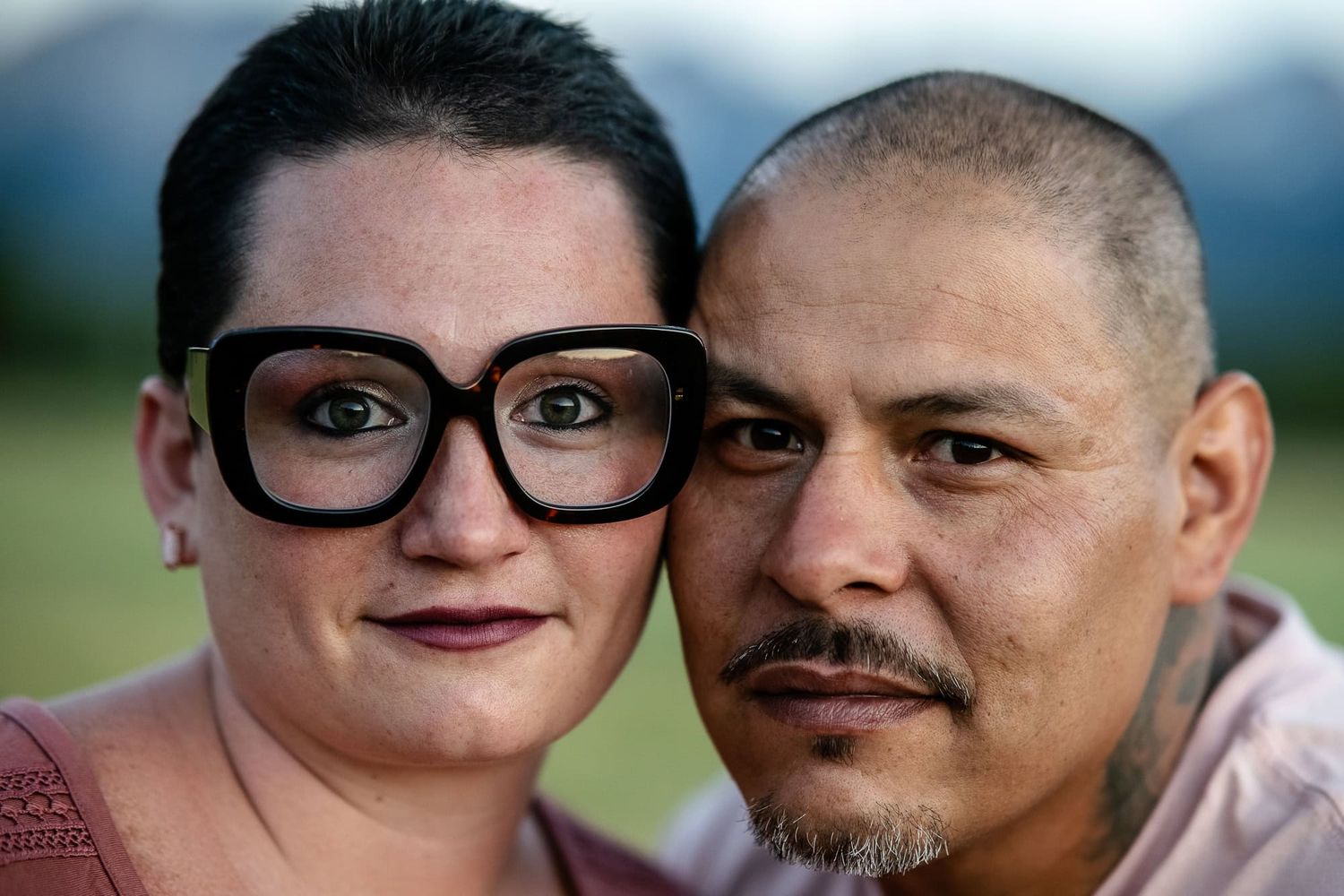 A close-up portrait of a couple outdoors with mountains in the soft-focus background.