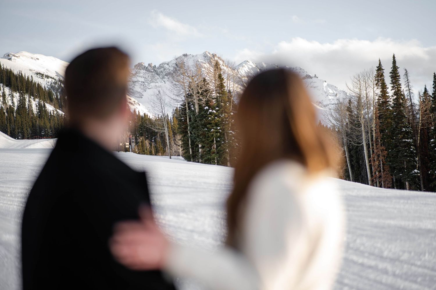 Silhouetted couple standing in snow with mountain peaks in background.
