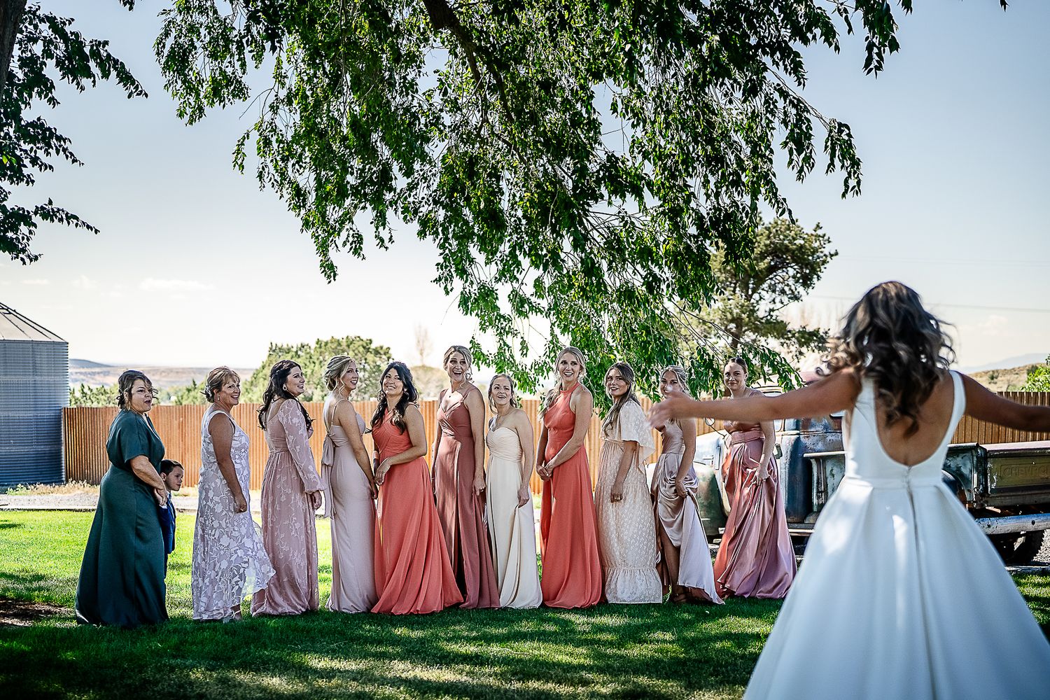 Bride poses with bridesmaids wearing colorful dresses at a rustic barn venue near Montrose Colorado.