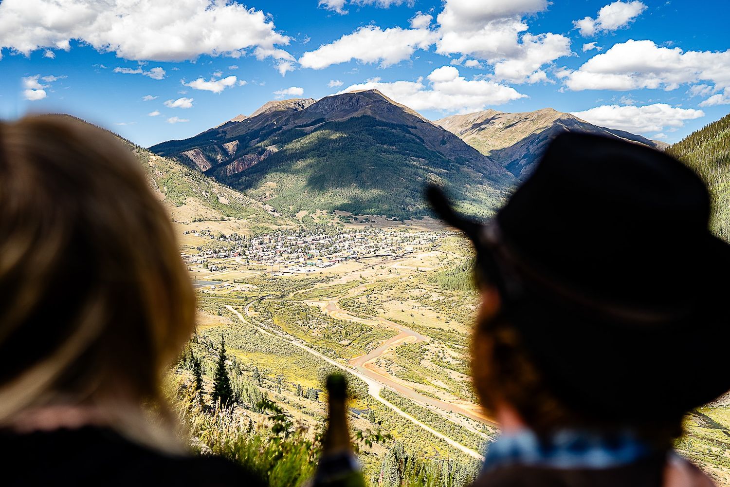 Scenic mountain valley view of a small town nestled between peaks under blue skies with white clouds.