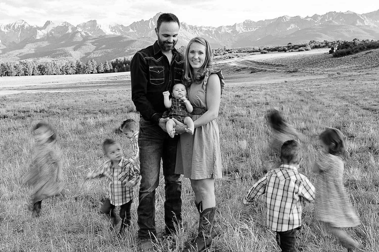 A family portrait with mountains in the background and motion-blurred children running around.