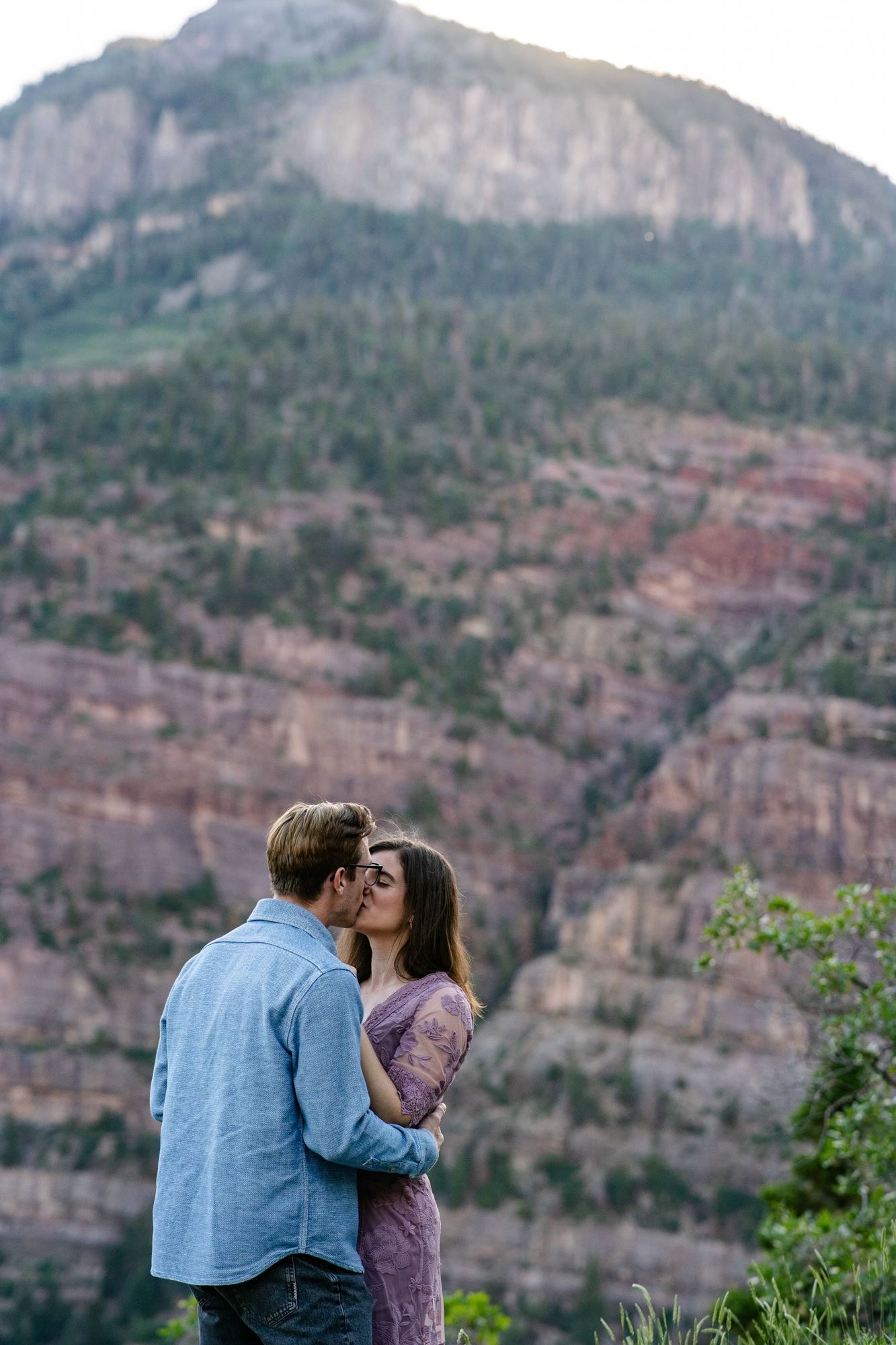 A couple embracing with dramatic red rock canyon cliffs forming a stunning natural backdrop.