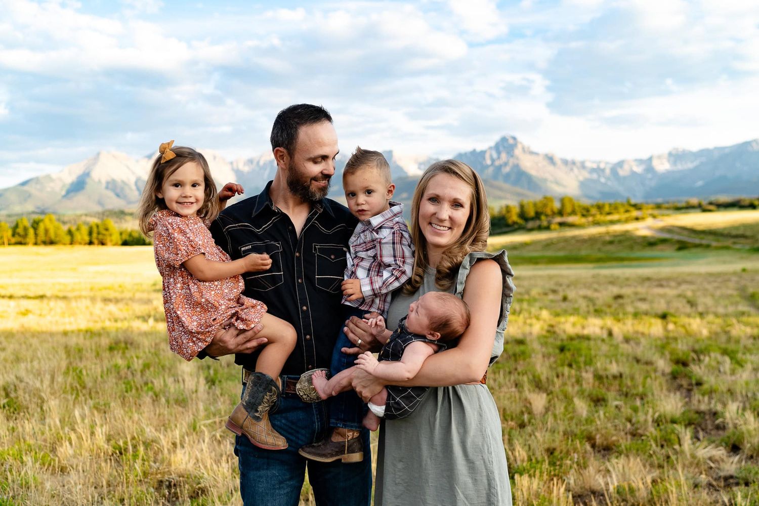 Family of four poses together in front of majestic mountain landscape.