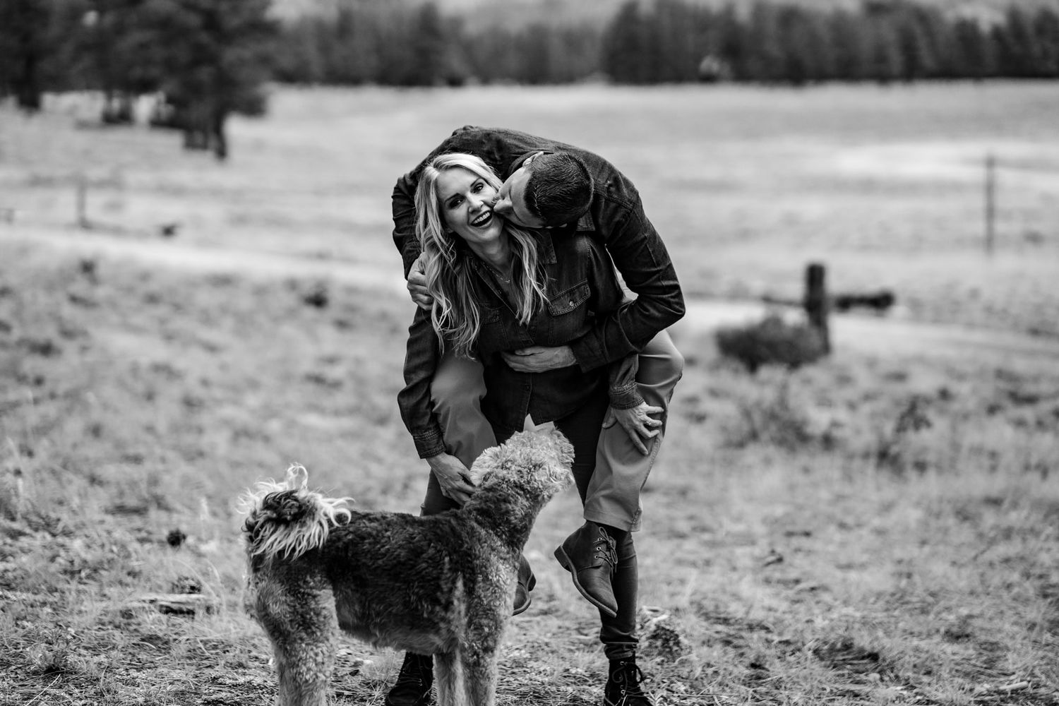 A person in dark clothing bends down to pet a shaggy dog in a black and white rural landscape.