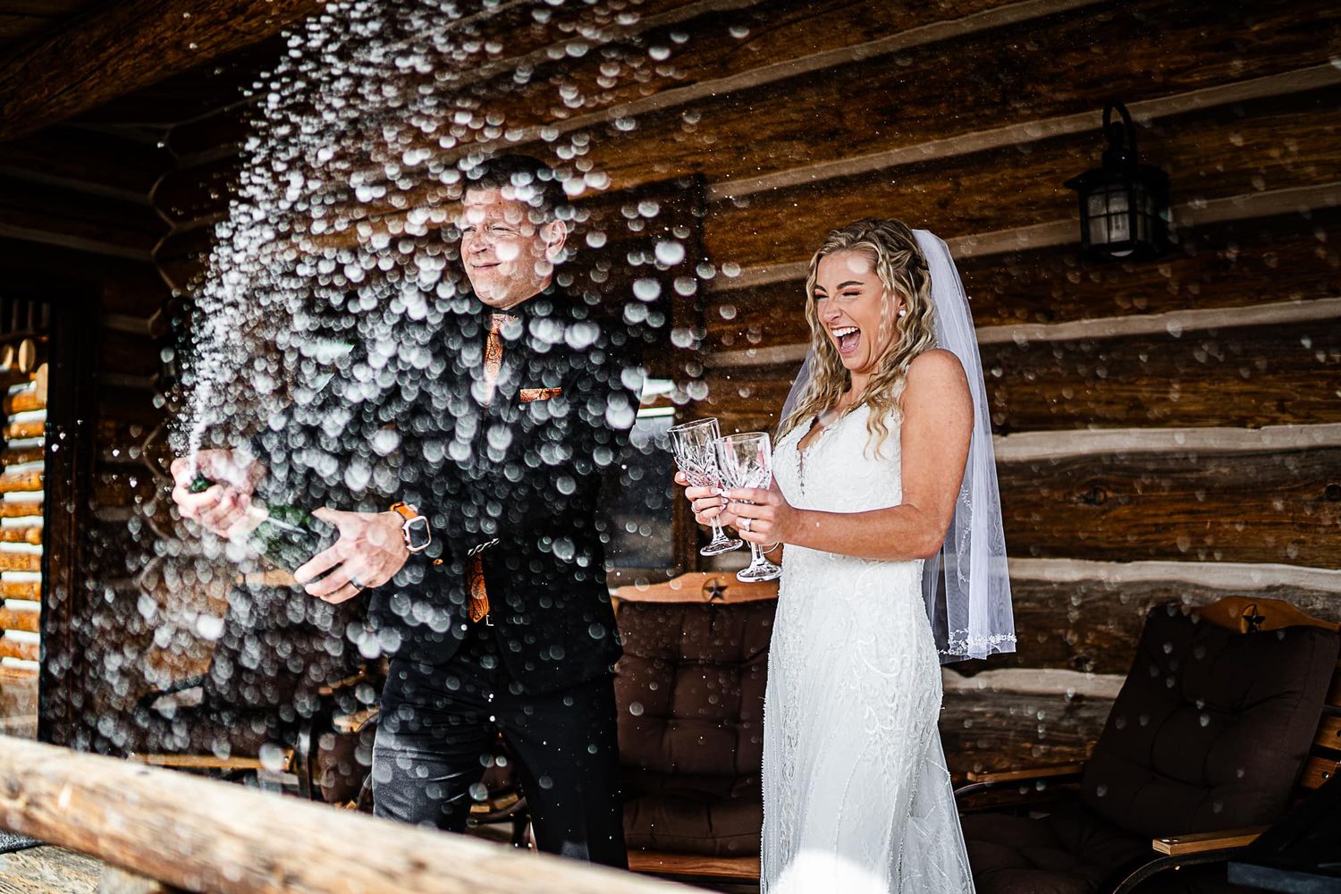 Couple celebrates with confetti shower against rustic log cabin backdrop.