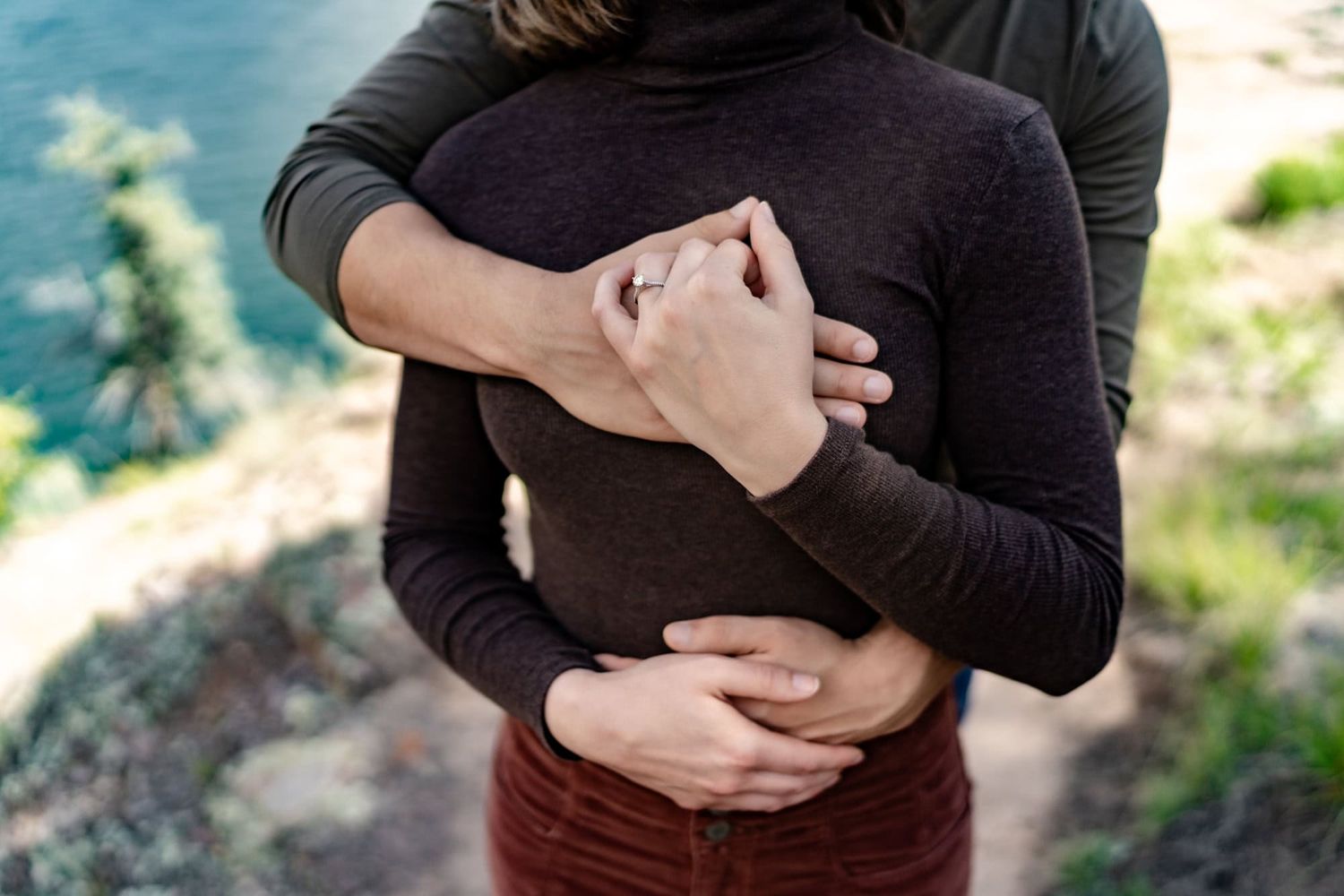 A couple sharing an intimate embrace outdoors wearing dark sweaters against a natural backdrop.