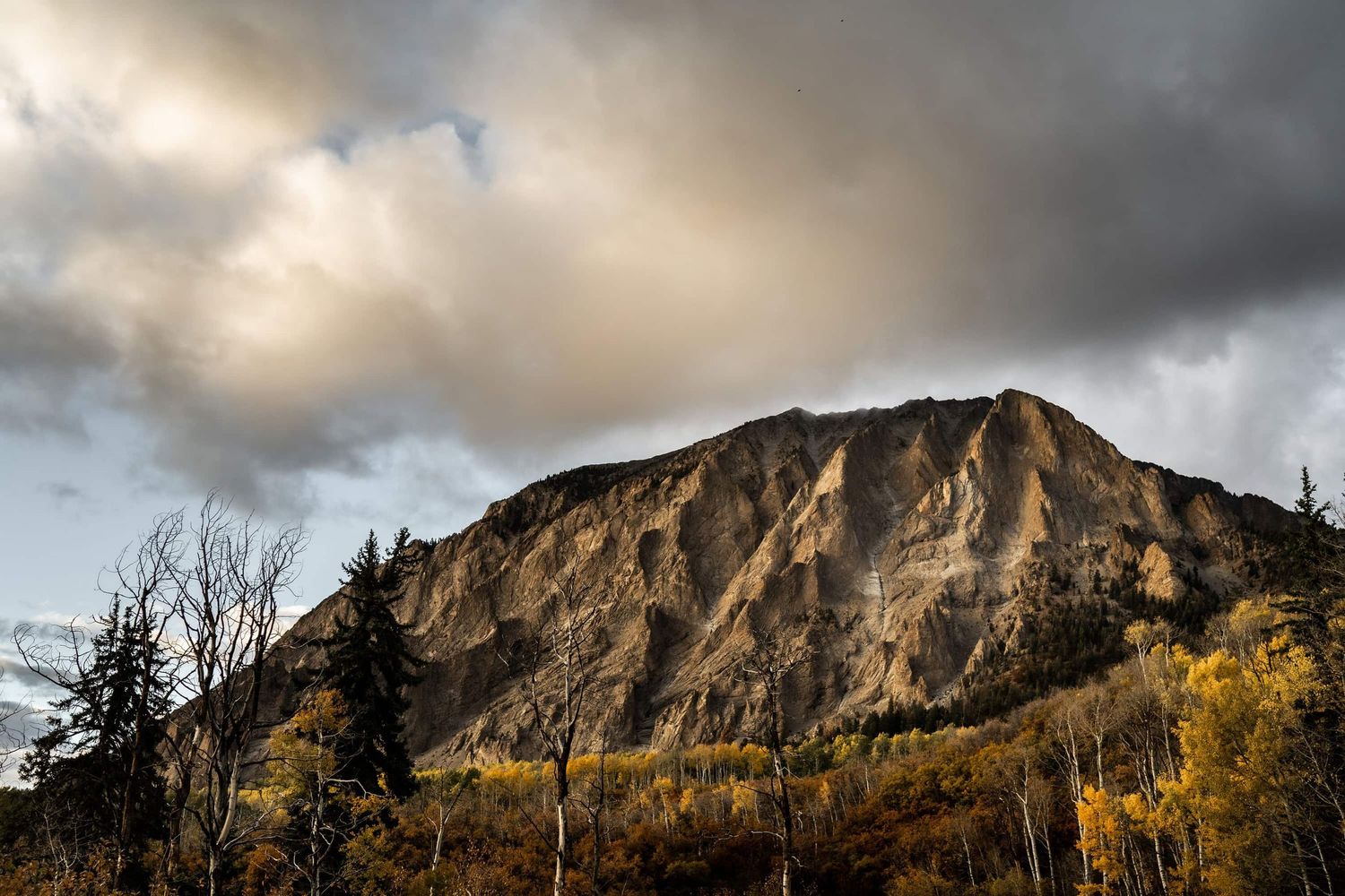 Dramatic mountain peak under stormy clouds during golden hour on Kebler pass in Colorado.