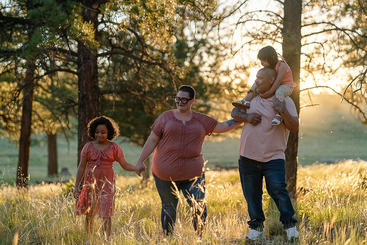 Family walking through sunlit forest meadow at golden hour.