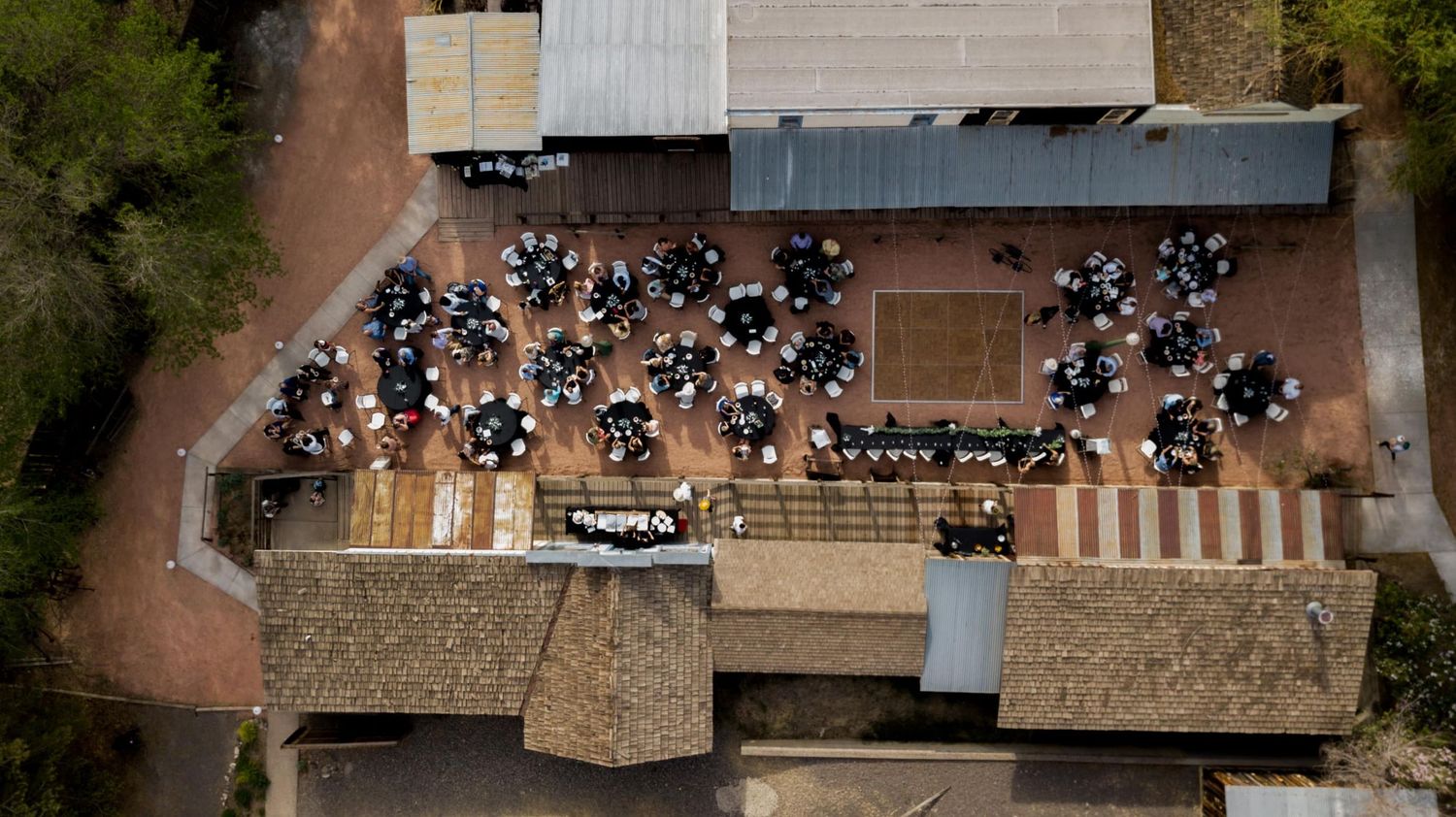 Birds eye view of outdoor wedding reception with guests seated at round tables.