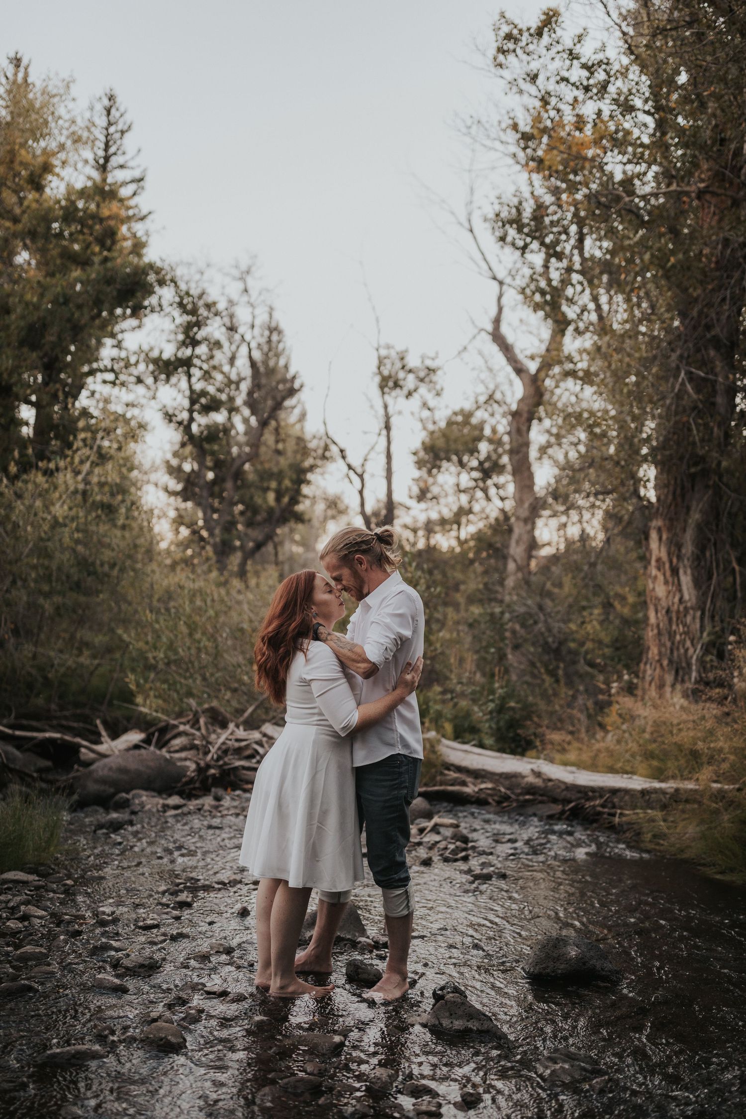 A romantic couple embraces in a rustic creek bed surrounded by autumn trees.