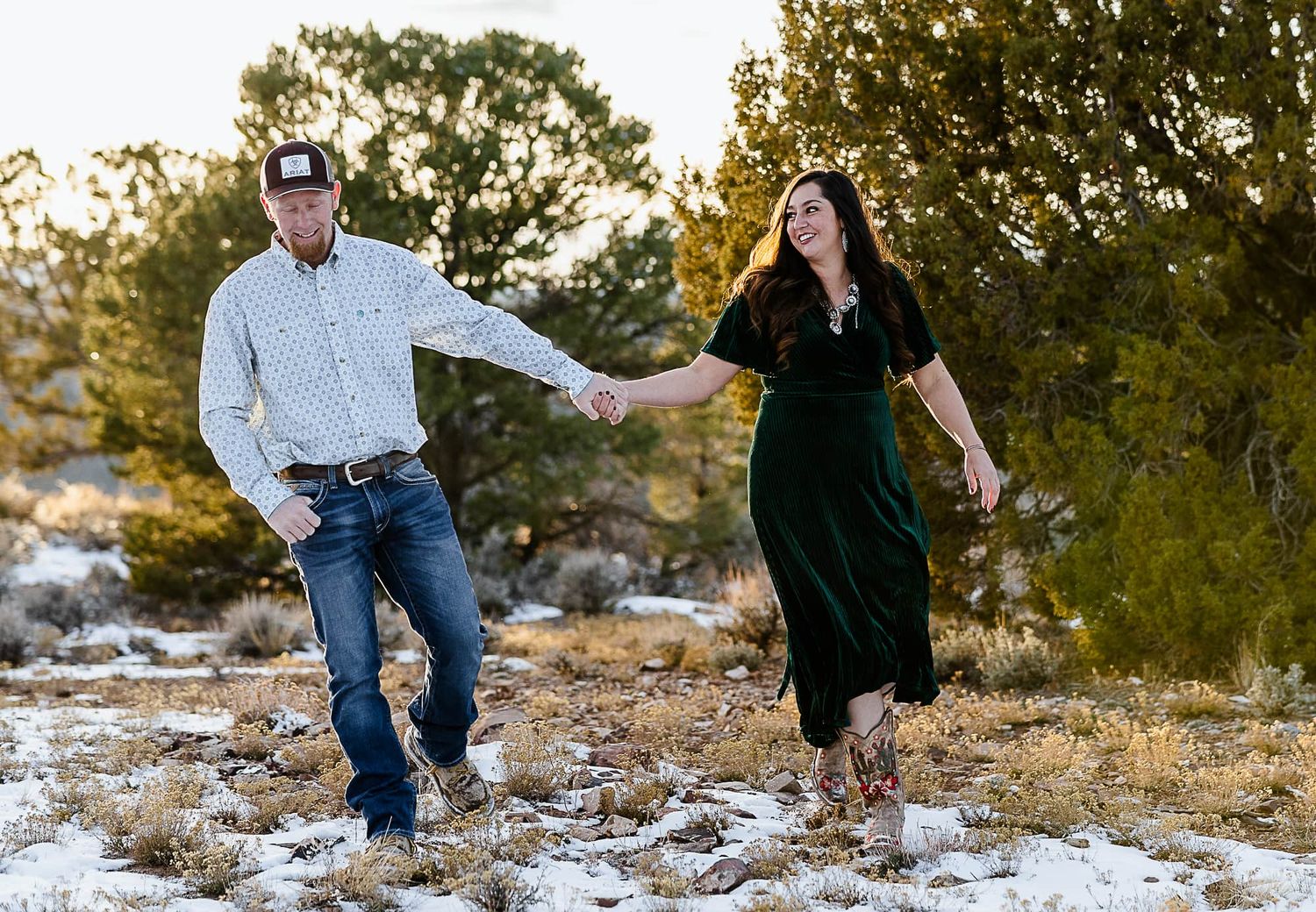 A couple walking hand in hand through a snowy landscape at golden hour.