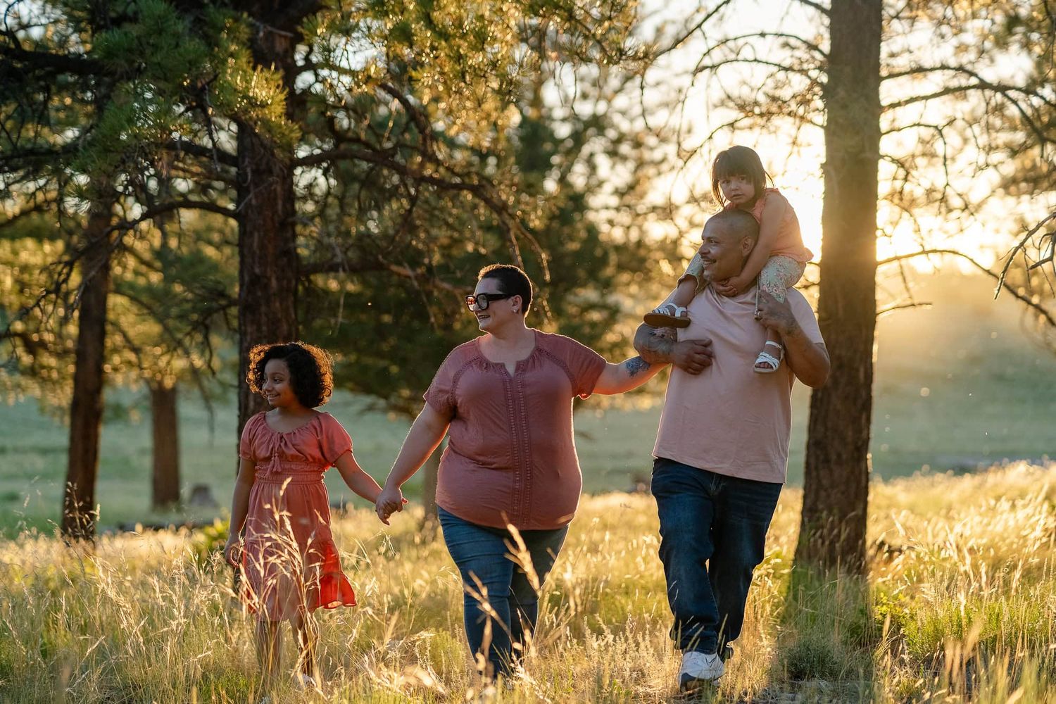 Family walking hand-in-hand through sunlit forest clearing at dusk.