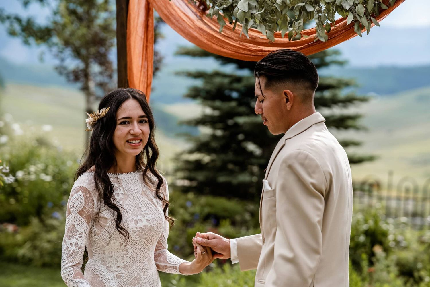 A couple exchanges rings during an outdoor wedding ceremony with scenic mountain views in the background.