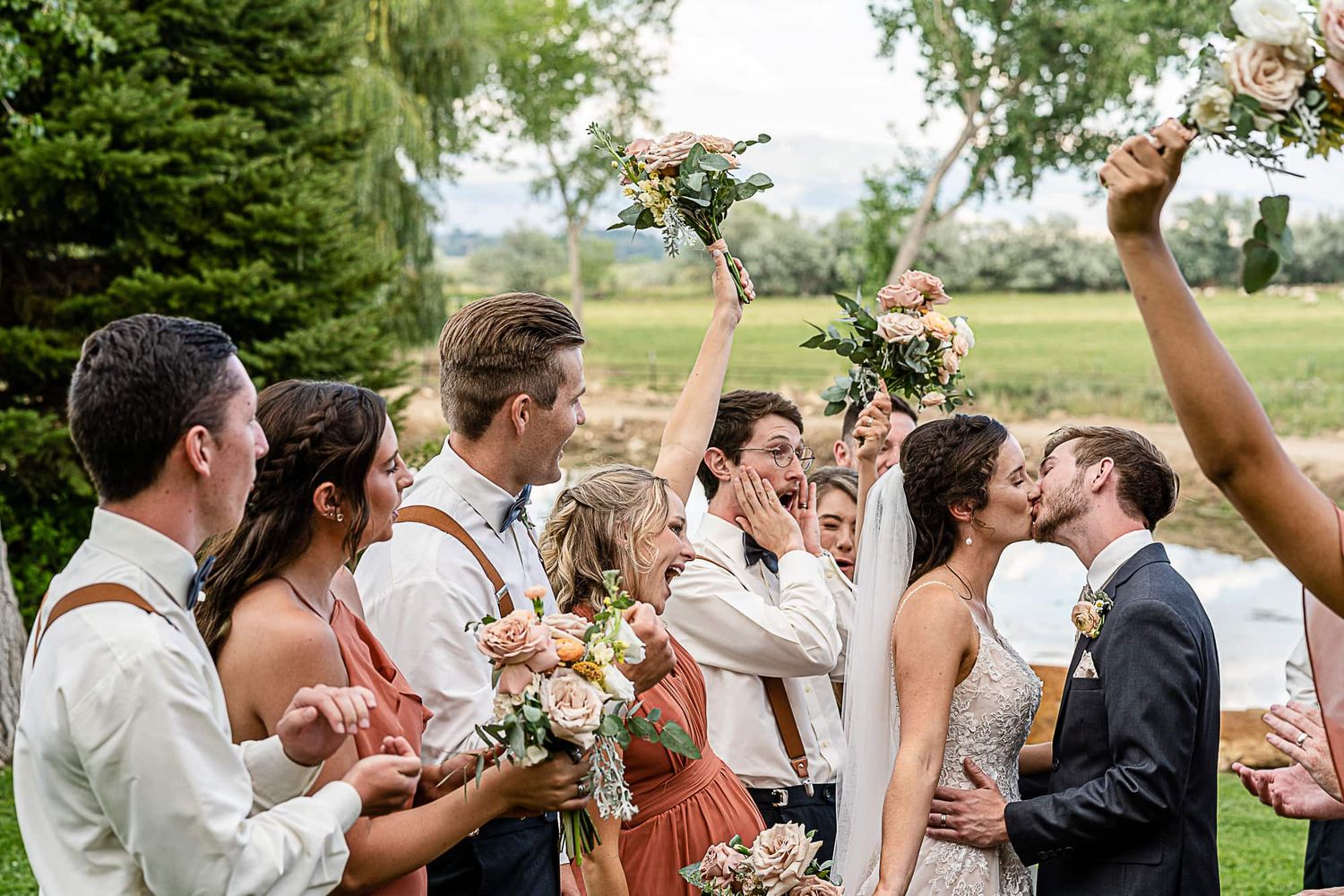 Wedding party celebrates with bouquets raised during outdoor garden ceremony.