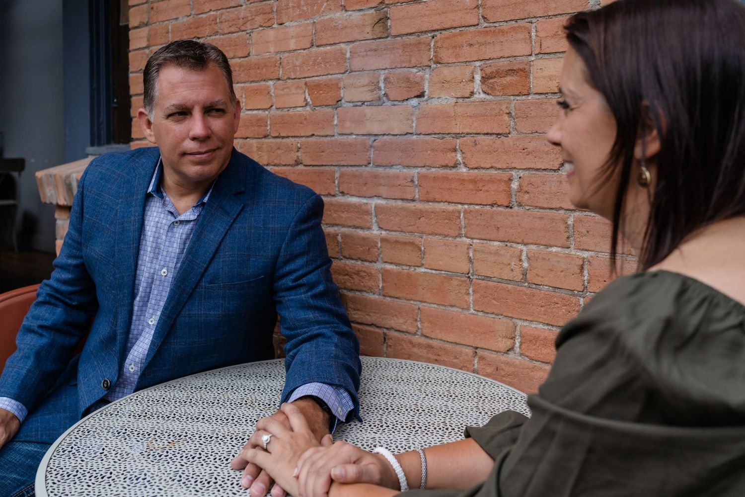 Couple having conversation at outdoor table against brick wall.