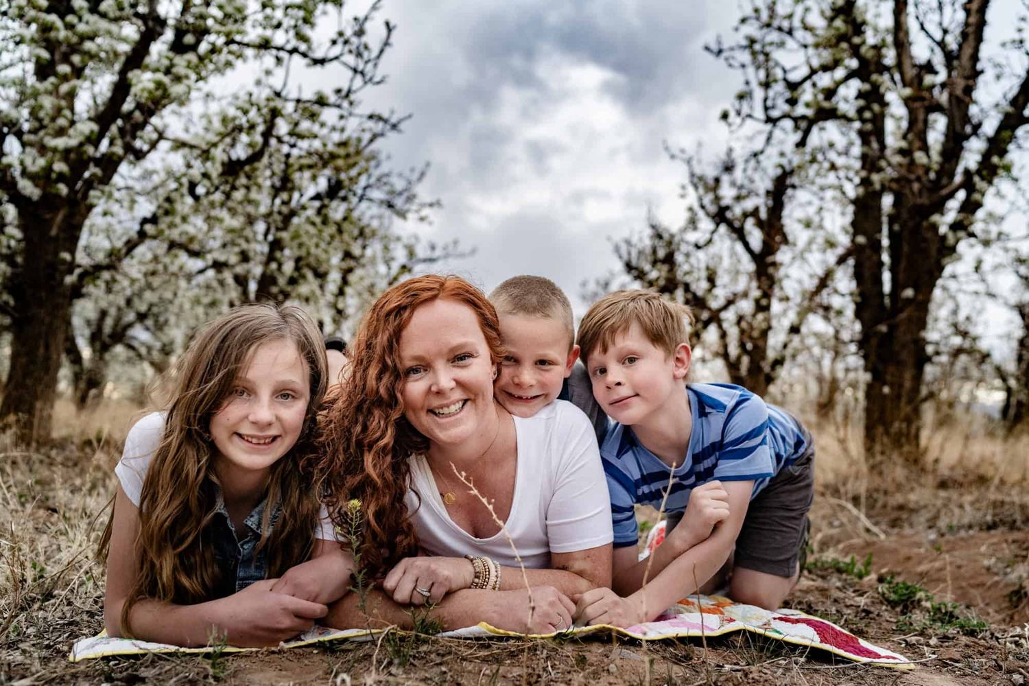 A joyful family moment captured on a blanket in an outdoor orchard setting.