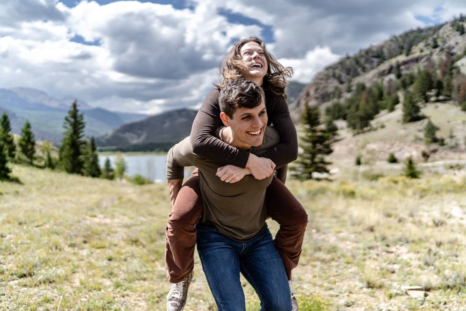 Playful piggyback ride along a scenic mountain trail with a lake view in the background.