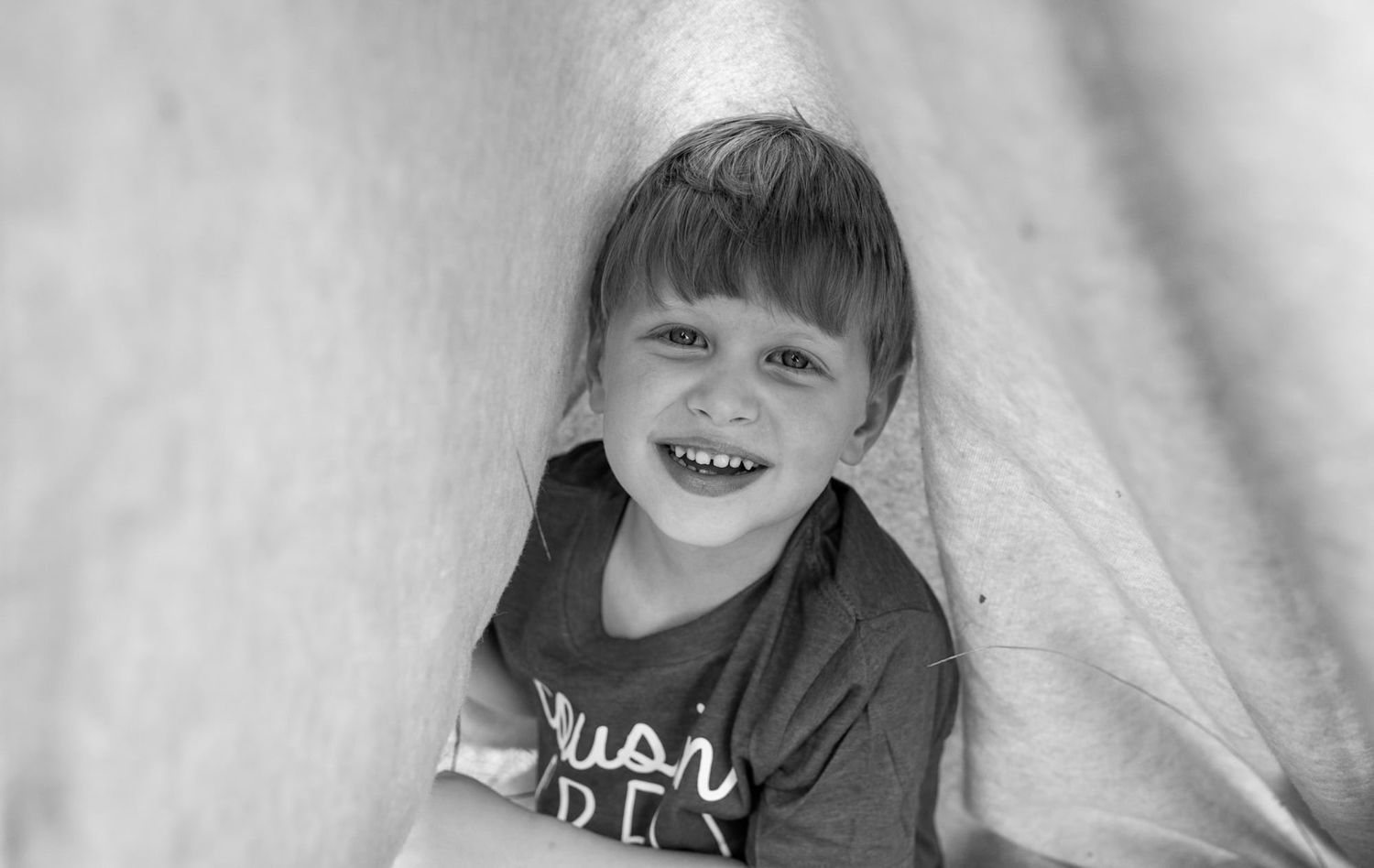 A black and white portrait of a smiling child against a light background.