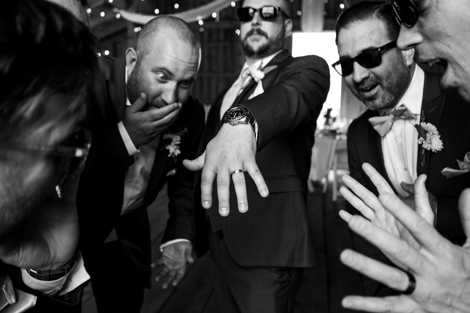 Group of men in formal attire examining rings and jewelry at a celebration.