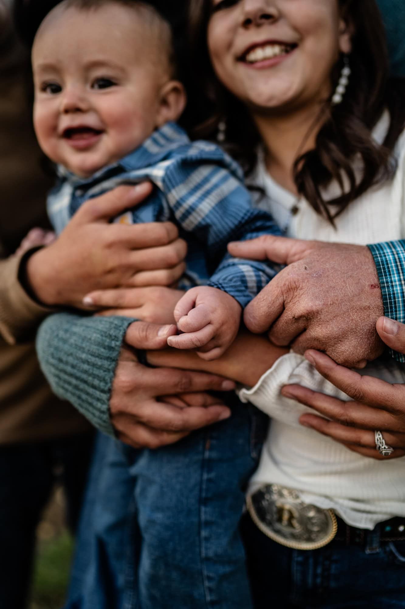 Close-up of hands joining together while holding infant wearing blue plaid shirt.