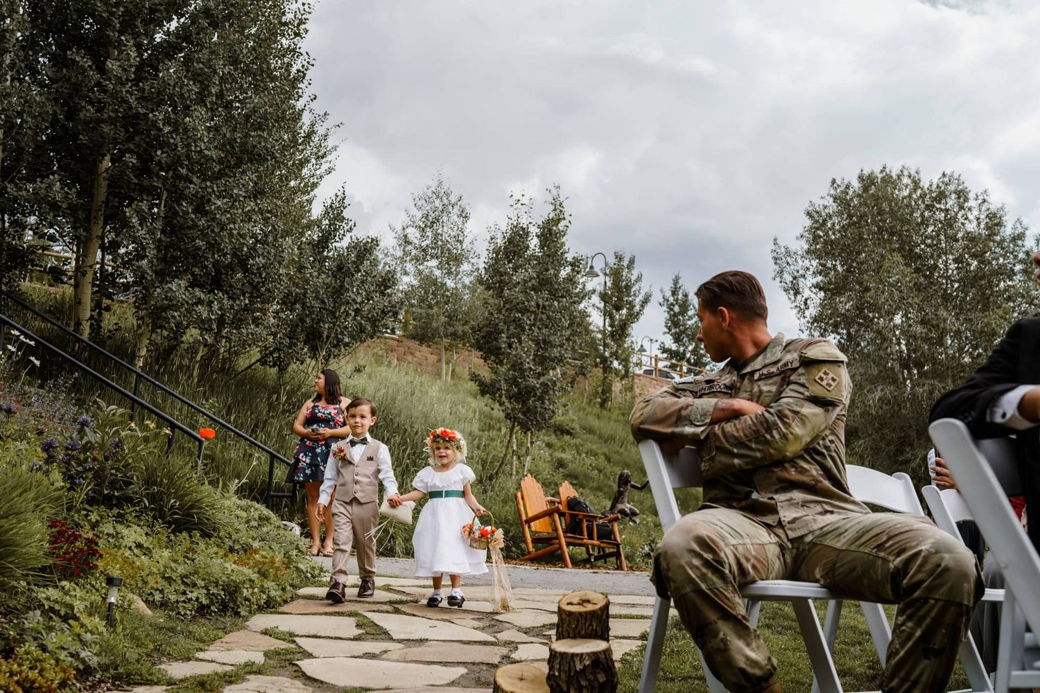 Musician playing an instrument along a garden path during an outdoor wedding ceremony.