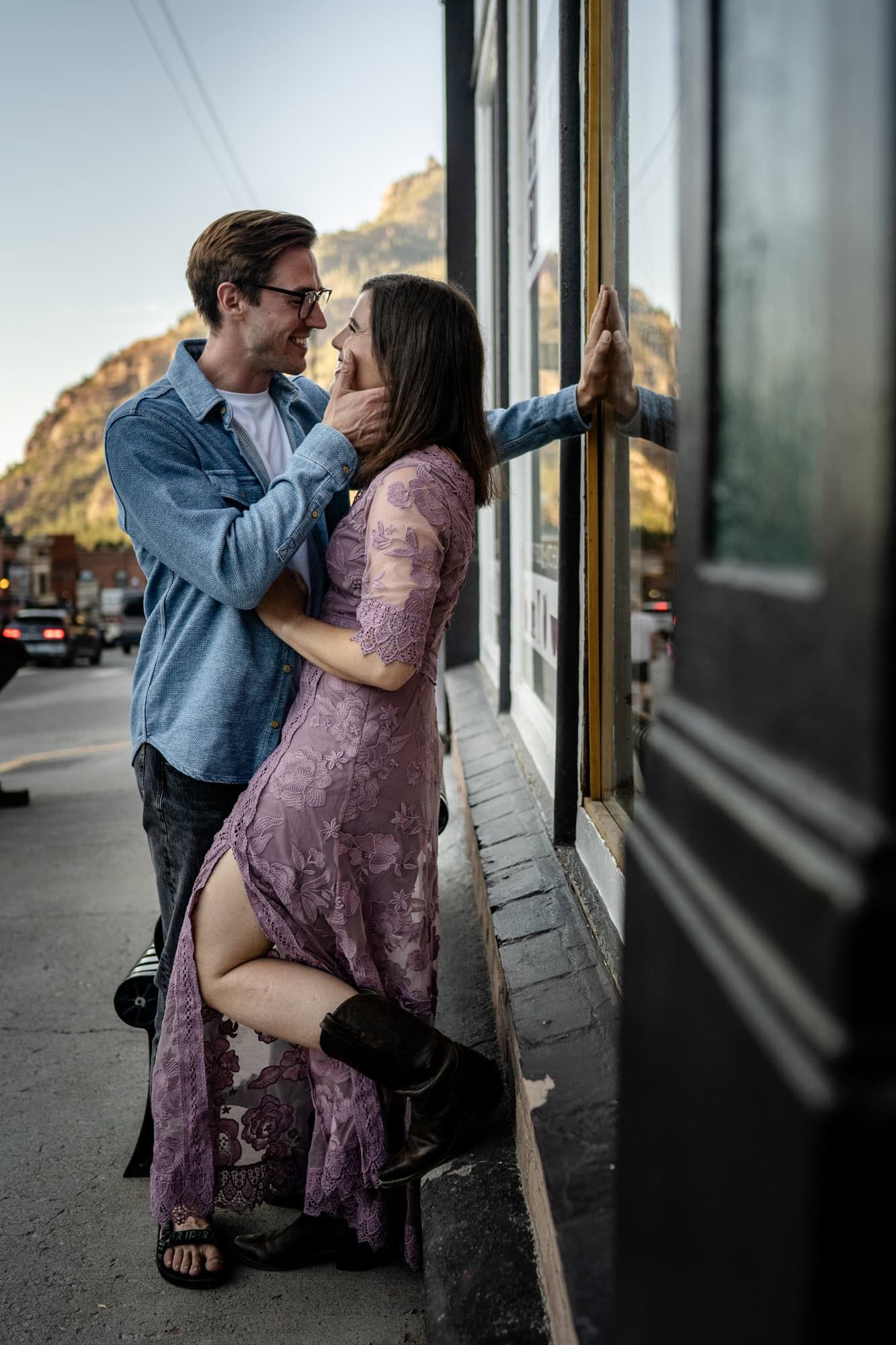 A couple in casual attire embracing outside a building with a mountain vista behind them.
