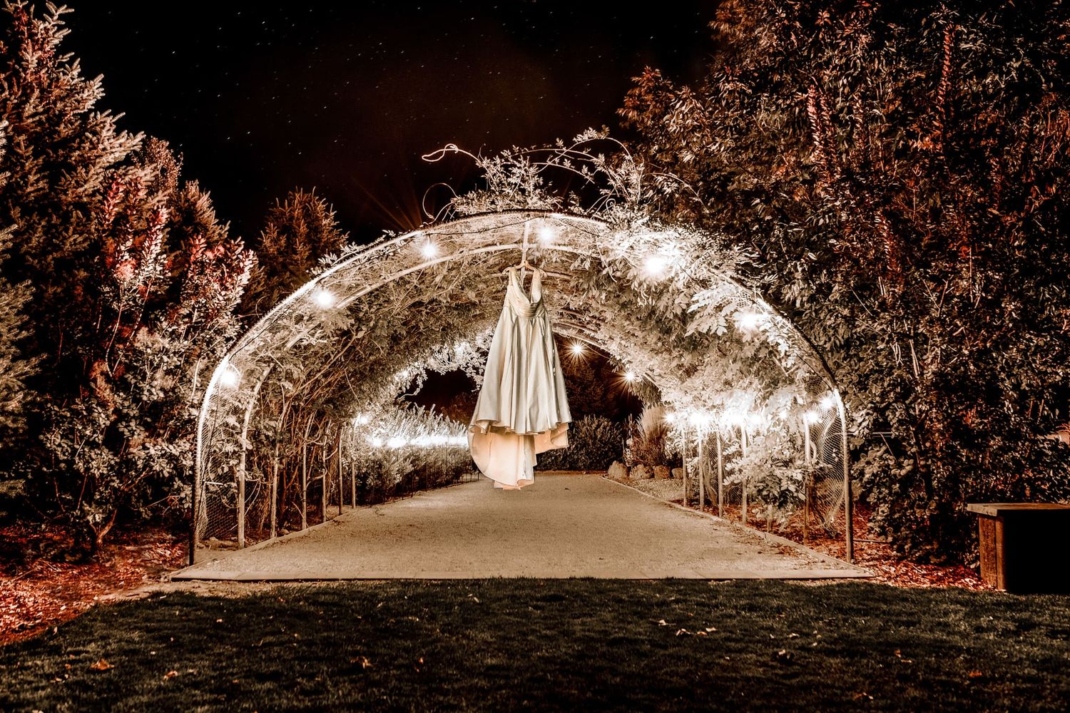 An illuminated wedding archway tunnel at night decorated with twinkling lights and white fabric.