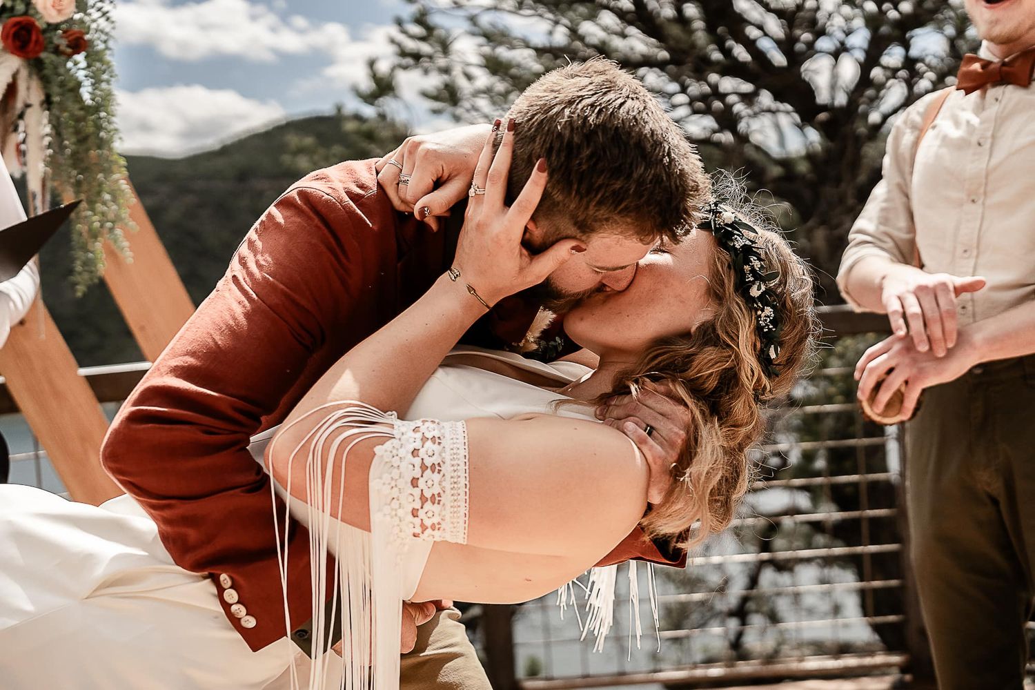 Couple shares passionate kiss during outdoor mountain wedding ceremony.