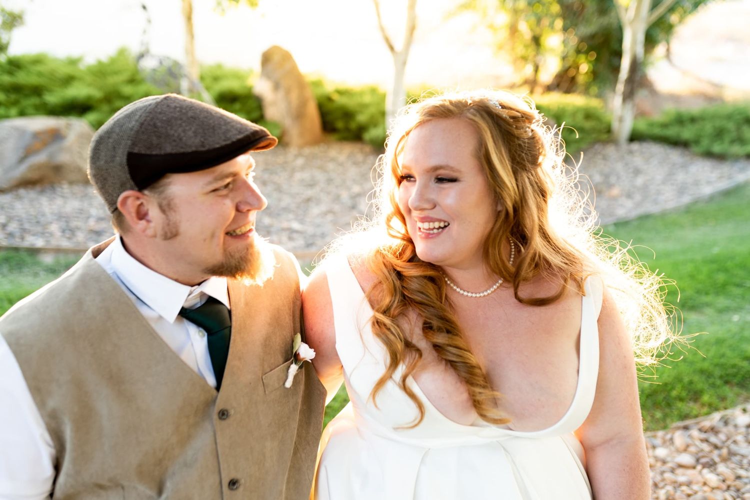 A joyful wedding couple shares a candid moment outdoors during golden hour.