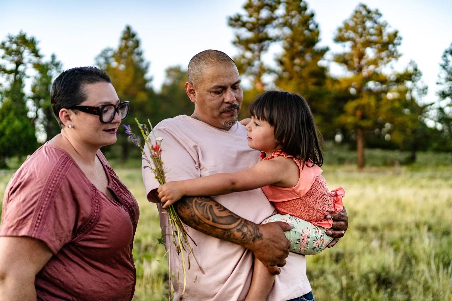 A family sharing an intimate moment together in a grassy field with evergreen trees.