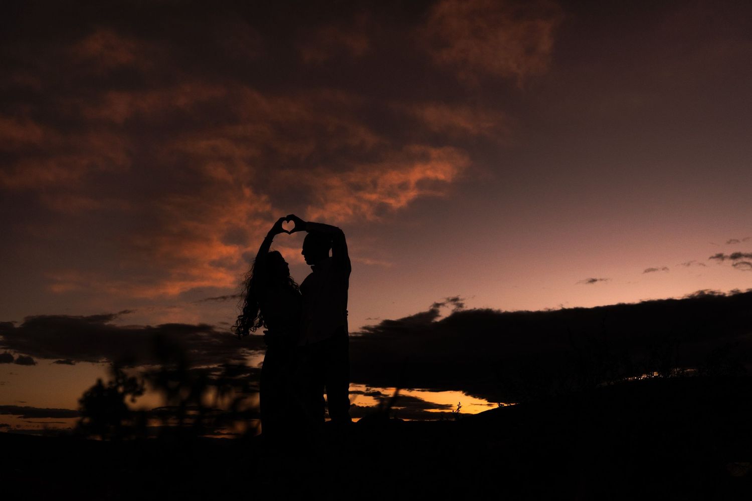 Romantic silhouette of couple embracing against colorful sunset backdrop.
