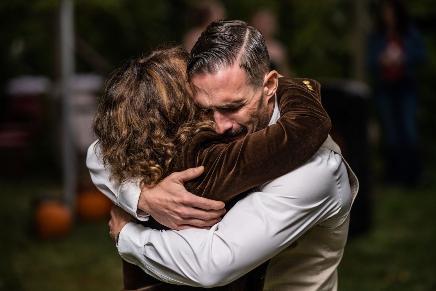Two people share an emotional embrace during outdoor wedding celebration.