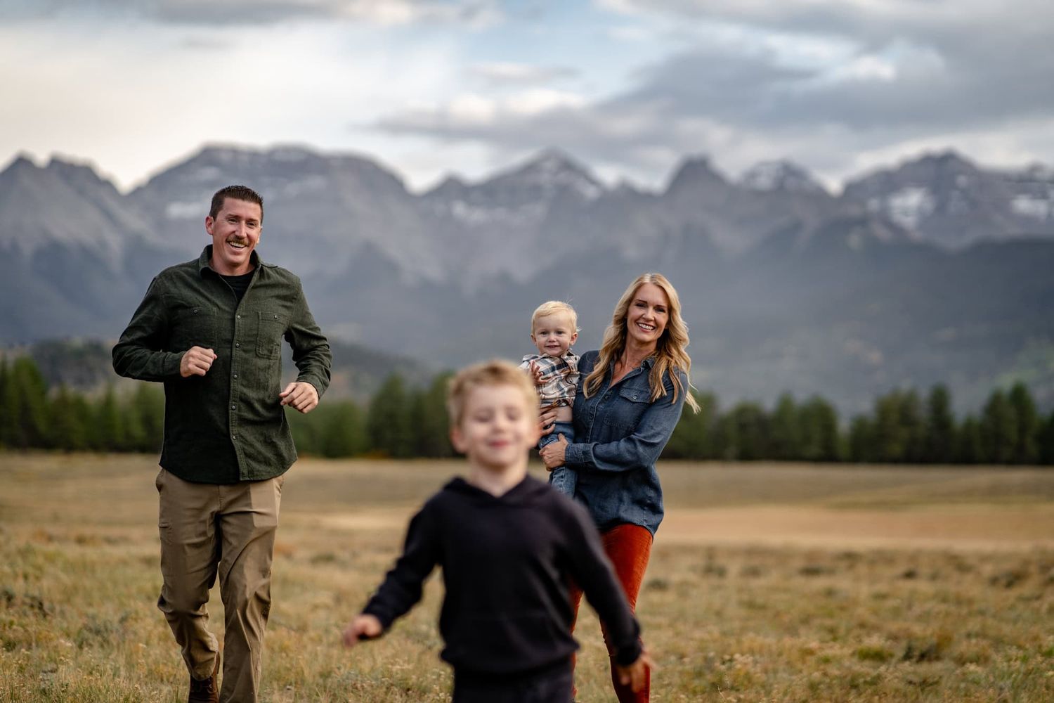 Family enjoying time together in an open field with majestic mountain ranges in the background.