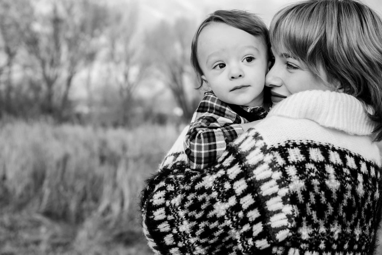 Black and white intimate portrait of parent and child in cozy winter sweaters against a natural background.
