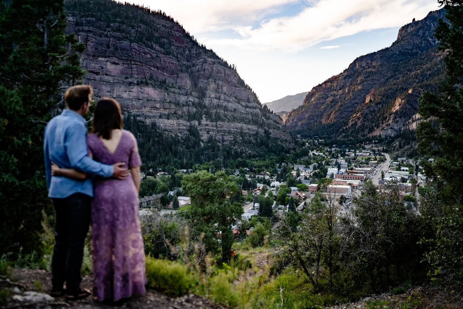 A couple overlooking a mountain valley town at sunset from a scenic viewpoint.