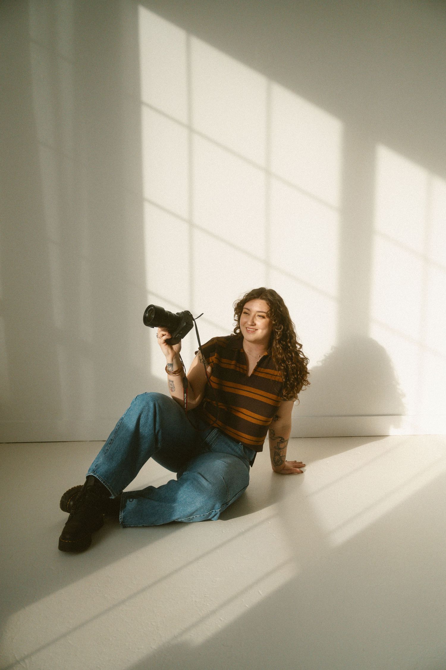 A person in casual clothing lies on a white floor as dramatic window light creates shadows in a minimalist setting.