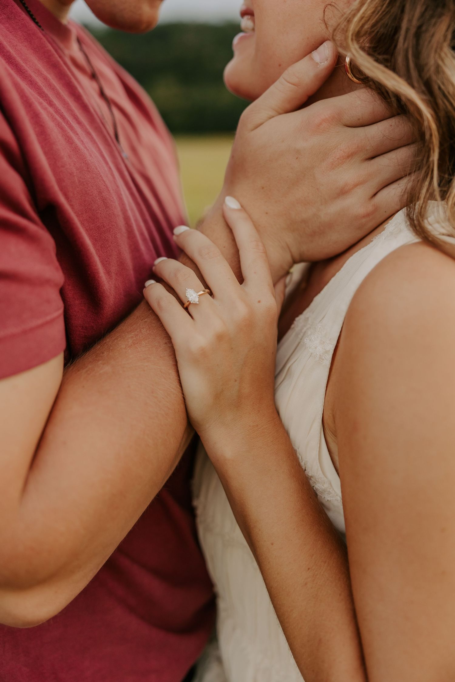 Close-up of engaged couple embracing outdoors, showcasing a delicate diamond engagement ring on her hand.