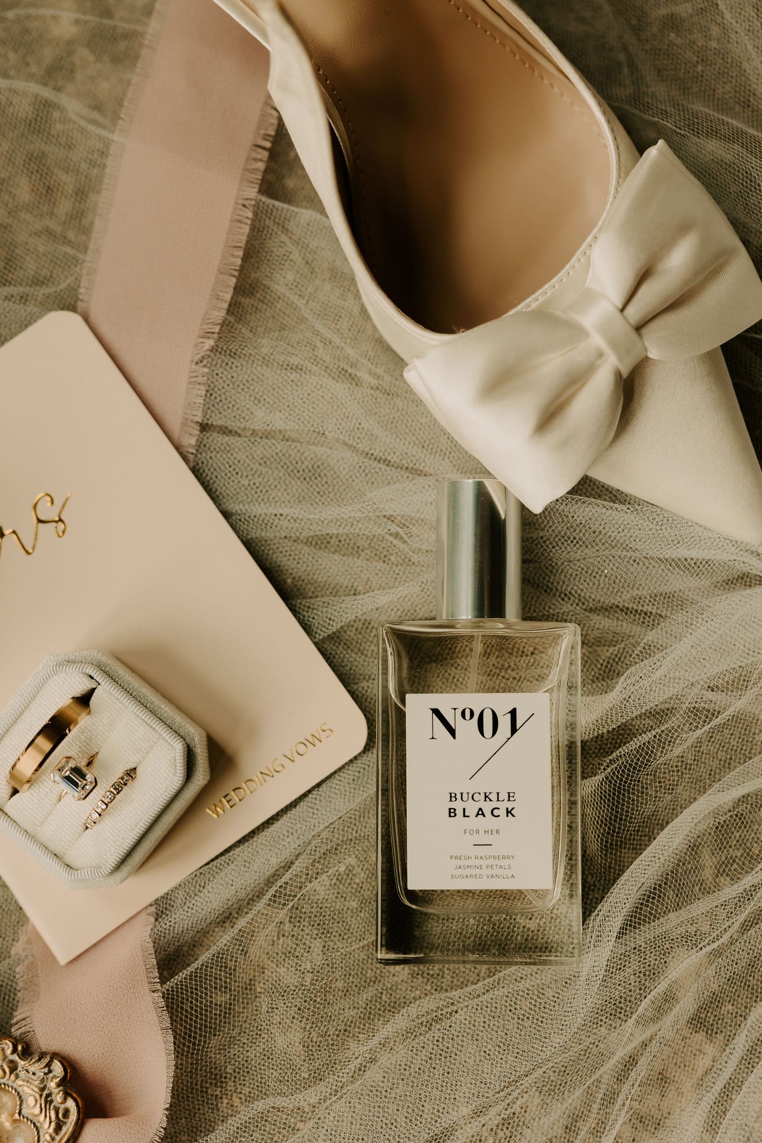 Elegant bridal flat lay featuring ivory bow heels, Buckle Black perfume, ring box, and veil details.