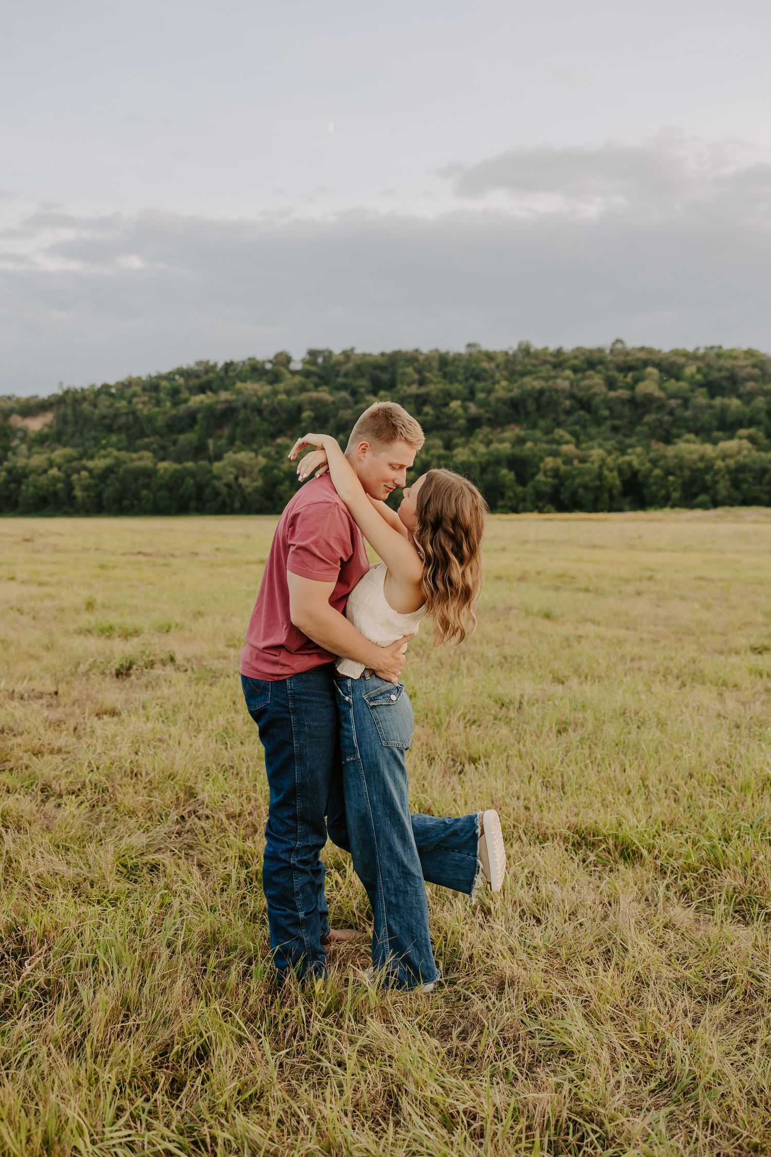Romantic couple embracing and kissing in an open green field with rolling hills in the background.