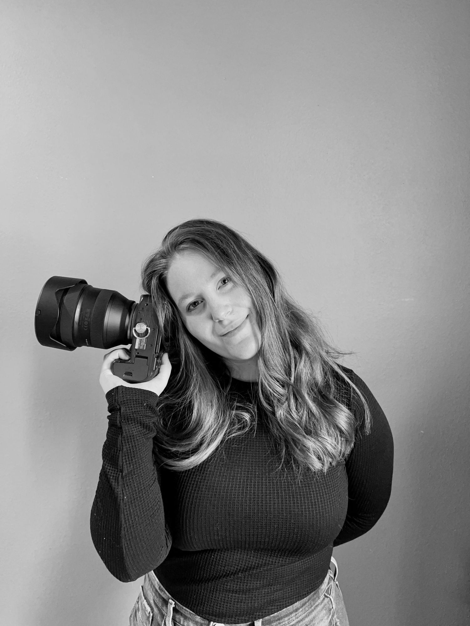 Black and white portrait of a female photographer holding a DSLR camera with a confident smile.
